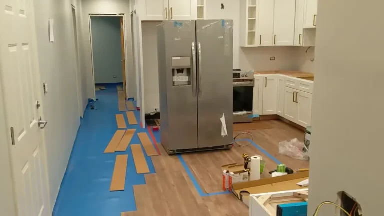 Wood-look luxury vinyl plank flooring installed throughout a kitchen with white cabinets and a stainless steel refrigerator