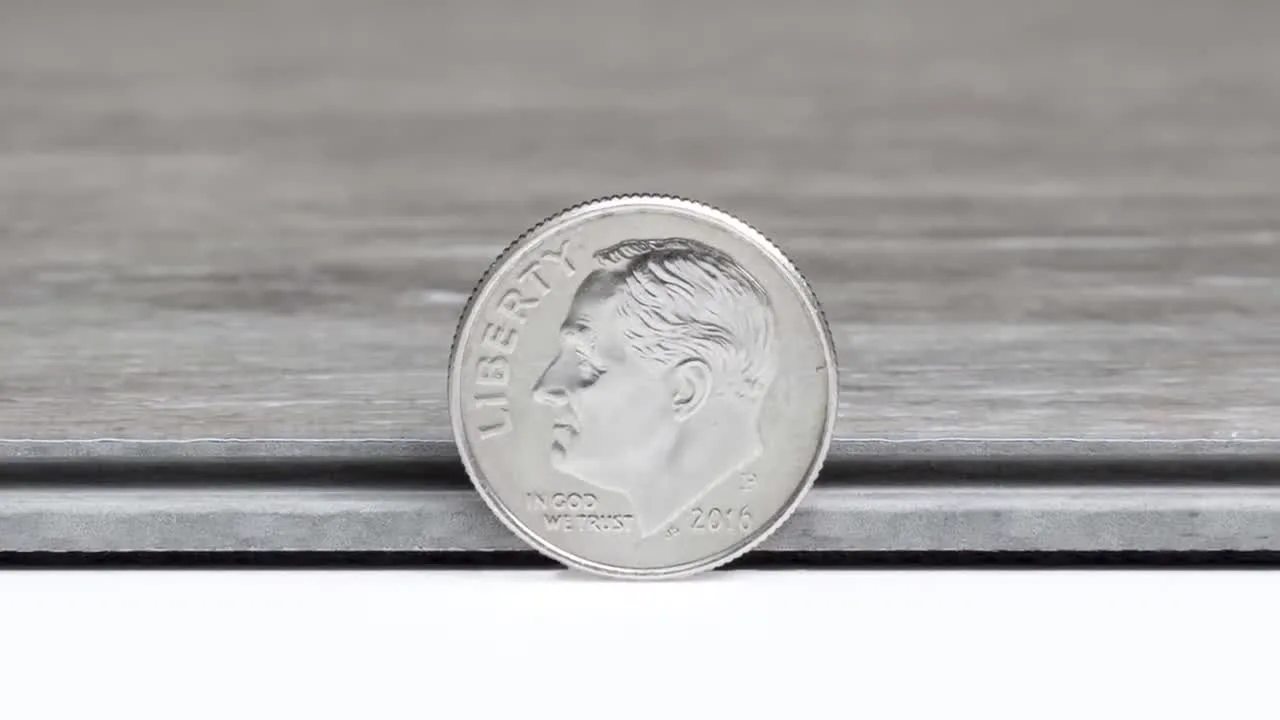 Close-up of the cut edge of a rigid core vinyl plank next to a dime for scale, showing the wear layer, printed wood layer, rigid core and backing